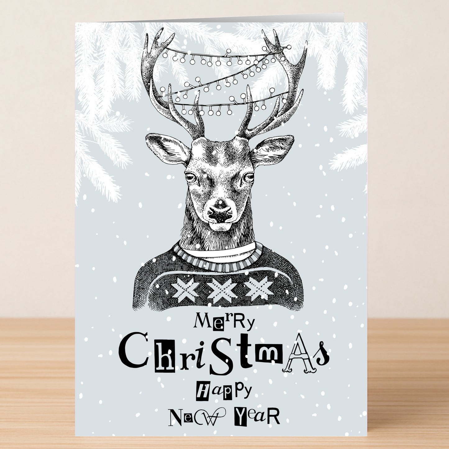 Send festive wishes with Twisted Gifts' Funky Reindeer Christmas Card—featuring an illustrated reindeer in a cozy sweater with string lights on its antlers, snowy branches, and "Merry Christmas Happy New Year" text.