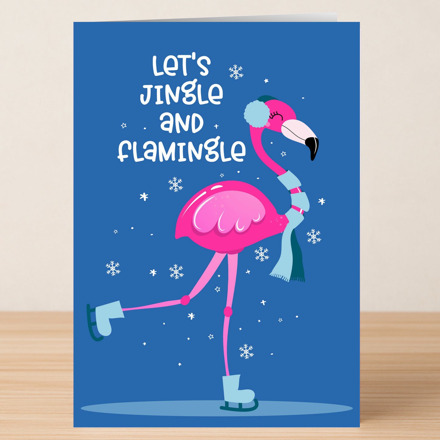 Send Christmas cheer with the Jingle Christmas Card from Twisted Gifts—a funny holiday card featuring a pink flamingo in winter gear ice skating, with "Let's Jingle and Flamingle" on a snowy blue background.