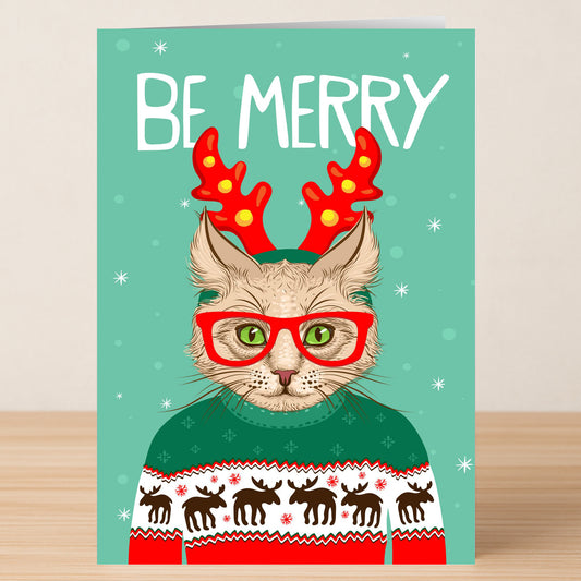 The Be Merry Christmas Card by Twisted Gifts features a cat in red antlers, glasses, and a Christmas jumper with "BE MERRY" at the top—a festive greeting for the season.