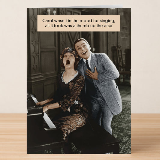 A woman at a piano reacts in surprise as a smiling man stands behind her, hand on chest. Humor text above jokes about her sudden mood shift. The Thumb Rude Greeting Card by Twisted Gifts is perfect for leaving a memorable impression!.