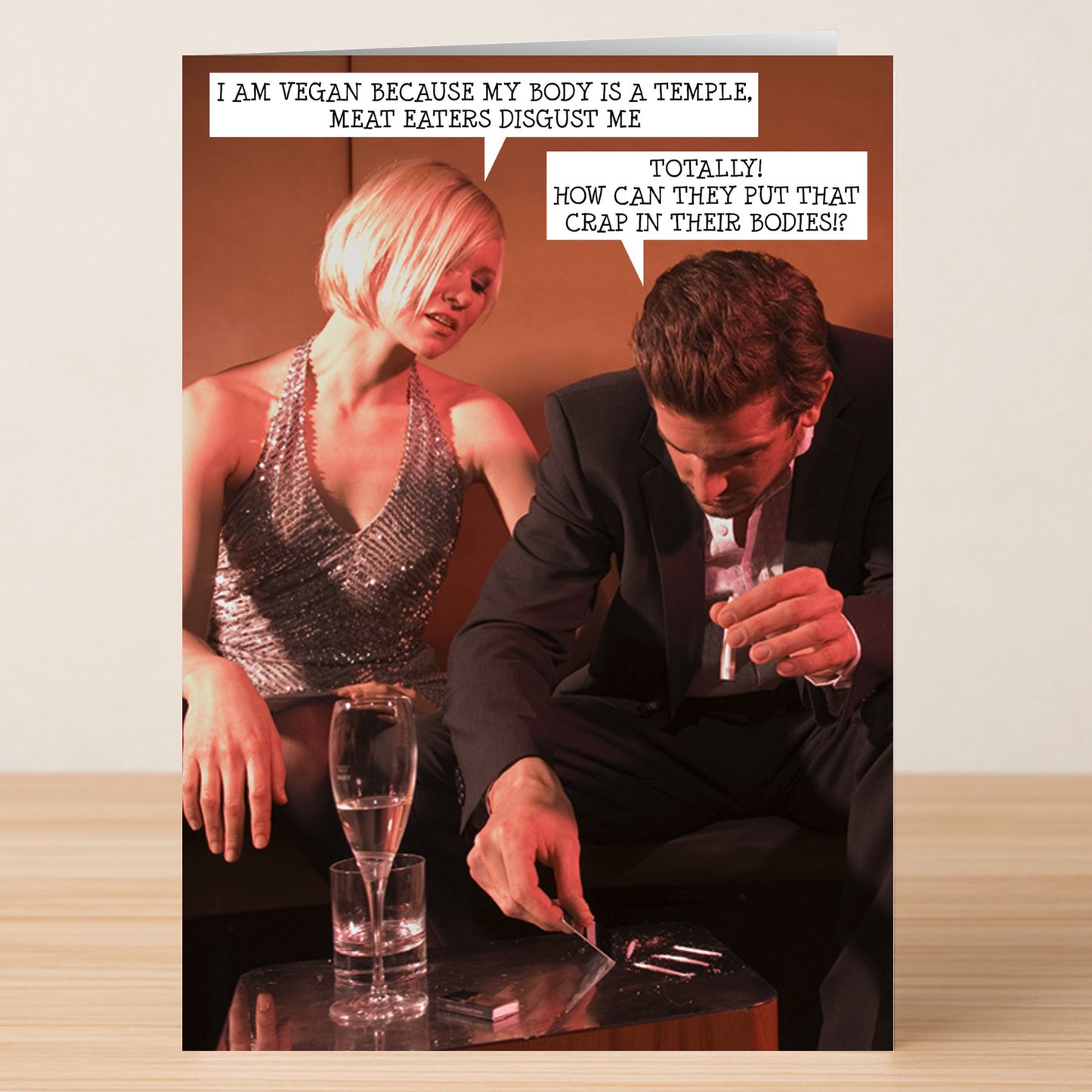 A woman and man exchange witty vegan jokes at a table, poking fun at meat lovers—making Twisted Gifts’ Meat Eaters Funny Greeting Card the perfect pick for anyone who loves humor and unique cards.