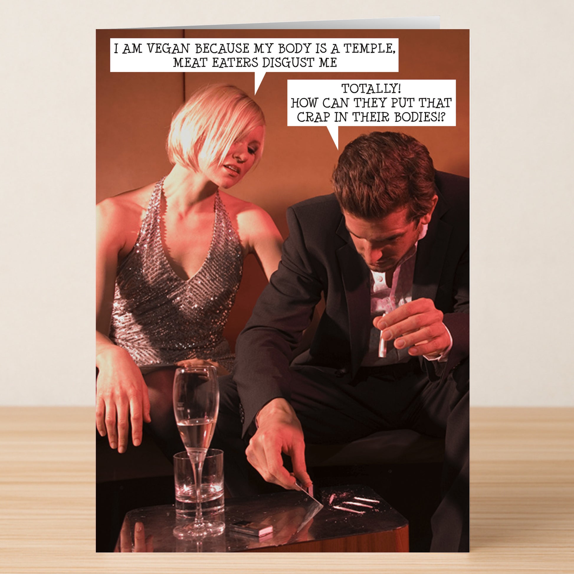 A woman and man exchange witty vegan jokes at a table, poking fun at meat lovers—making Twisted Gifts’ Meat Eaters Funny Greeting Card the perfect pick for anyone who loves humor and unique cards.