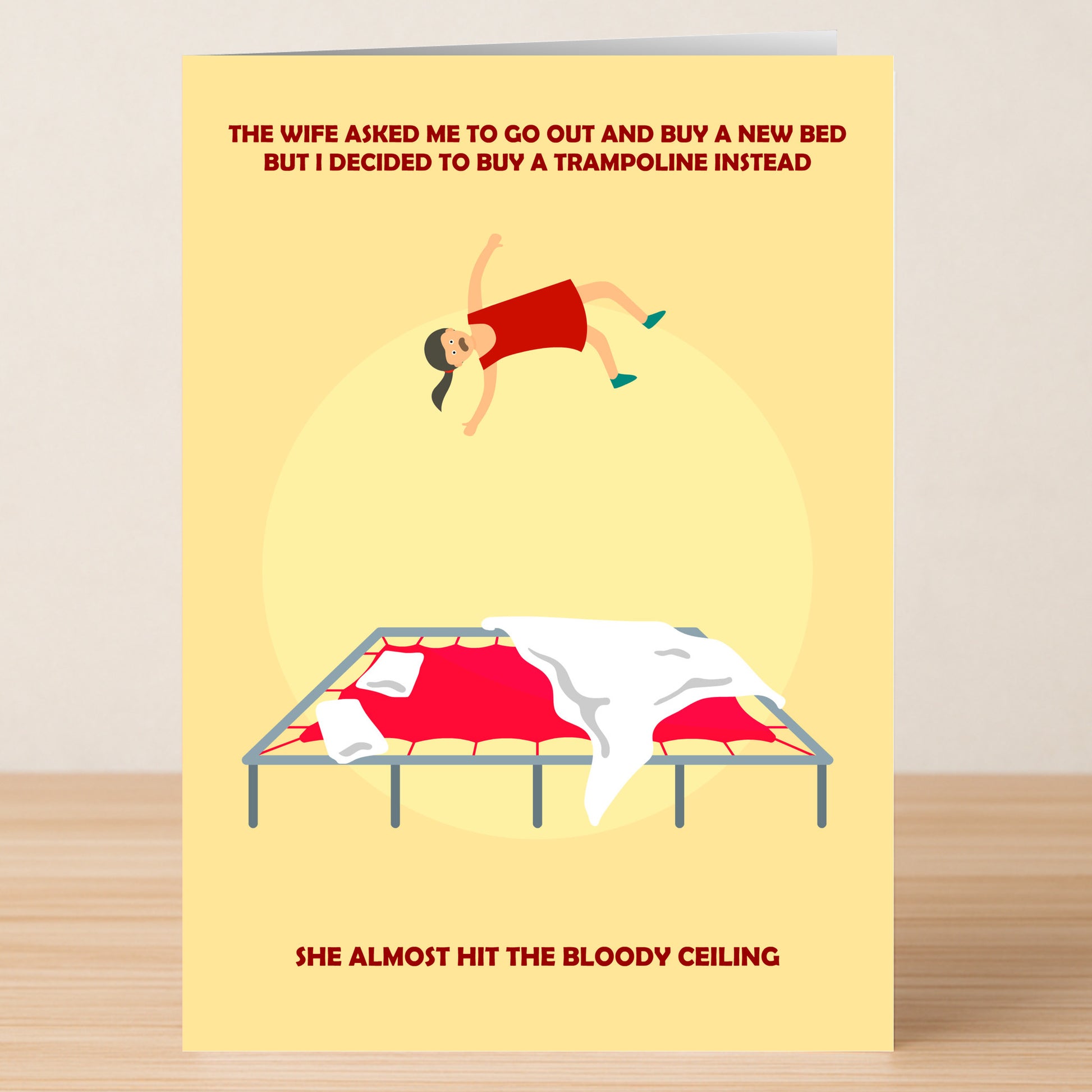 The Trampoline Funny Greeting Card from Twisted Gifts shows a cartoon woman bouncing on bed sheets, humorously suggesting a trampoline adds extra spring to her step over an ordinary bed.