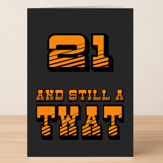 The Twisted Gifts 21 - Still A Twat Insulting Birthday Card features bold orange and black text on a dark background—an ideal, quirky 21st birthday insult card shown upright on a wooden surface.