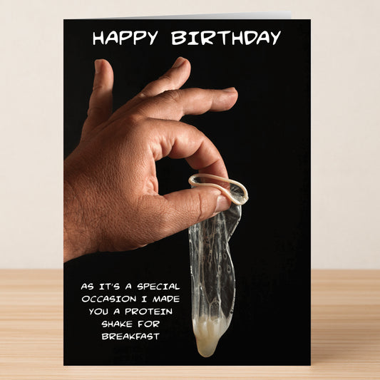 A hand holds a used condom against a black background on the Twisted Gifts Protein Shake Rude Birthday Card, which jokes about enjoying a "protein shake for breakfast"—ideal for fitness lovers with an edgy sense of humor.