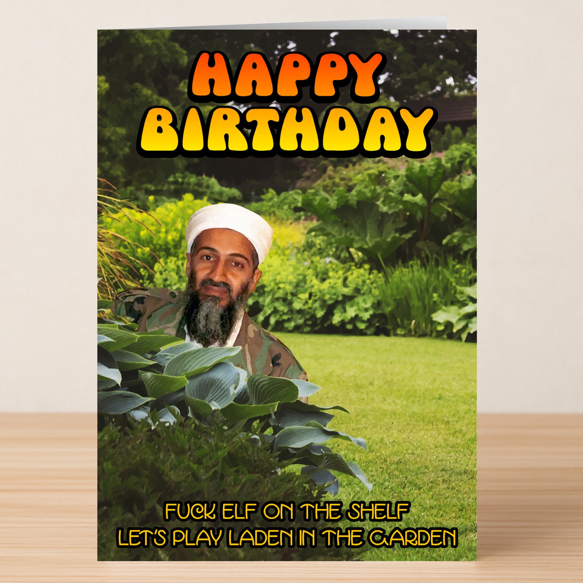 The Laden Garden Funny Birthday Card by Twisted Gifts features bold "Happy Birthday" text and a cheeky man hiding in a garden with the caption, "Fuck elf on the shelf, let's play Laden in the garden." Ideal for a memorable birthday.