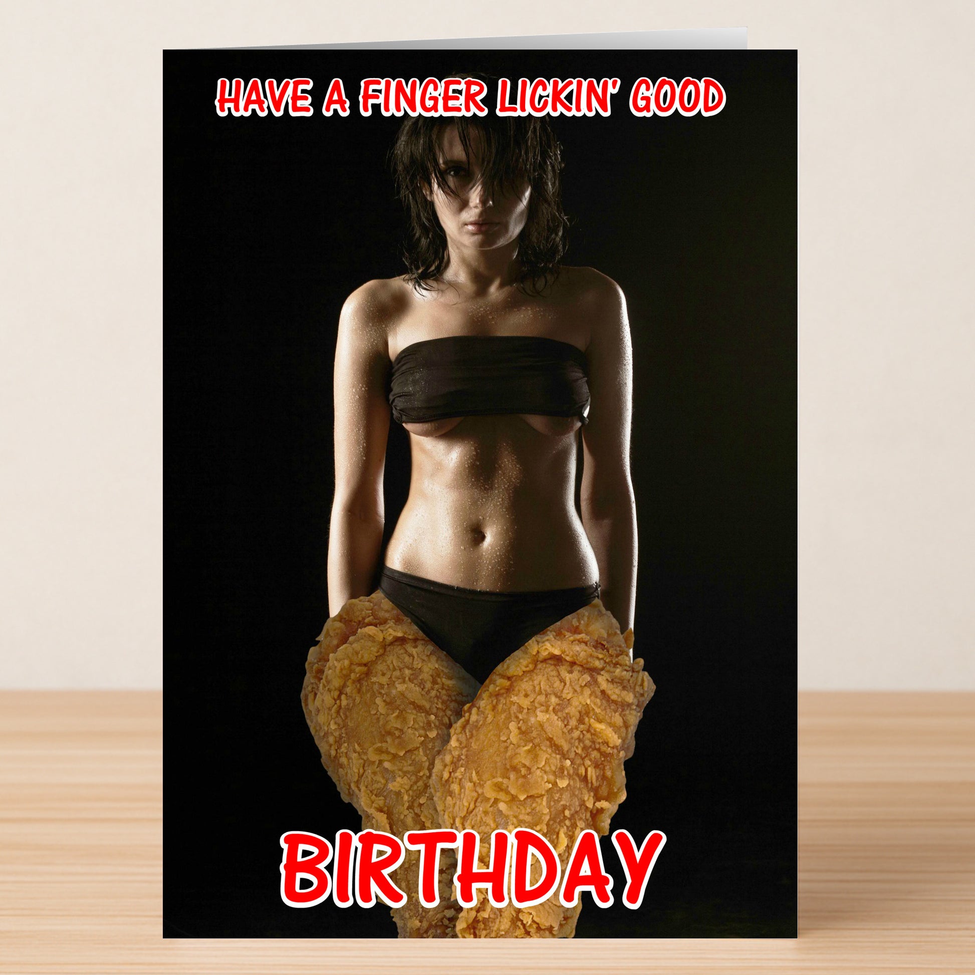 The Finger Licking Funny Birthday Card by Twisted Gifts features a woman in a dark bikini with giant fried chicken drumsticks edited over her hips and the text "Have a finger lickin' good birthday." Ideal for anyone who loves humorous birthday cards.