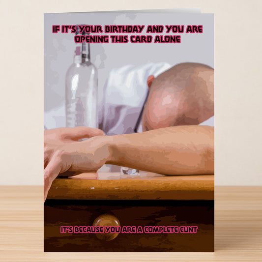 A person slumped over a table with bottle and glass, featuring Twisted Gifts’ Complete Cunt Insulting Birthday Card that reads: "If it's your birthday and you are opening this card alone it's because you are a complete cunt.