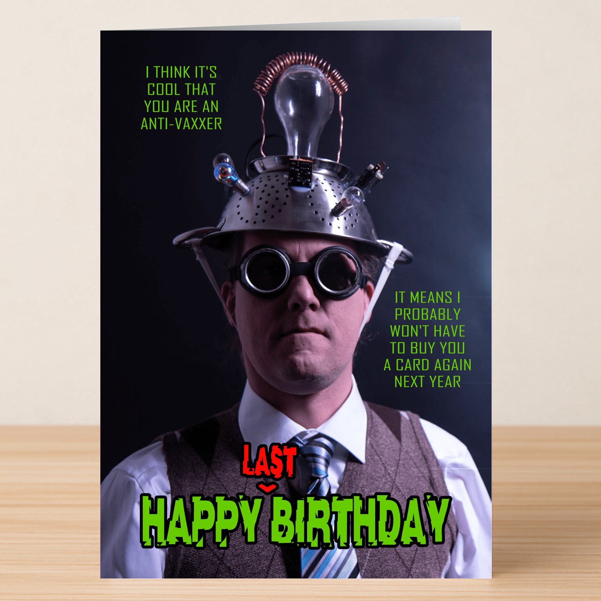 A man in a suit, goggles, and a wired colander hat stands before the Twisted Gifts Anti-vaxxer Funny Birthday Card, known for its sarcastic humor.