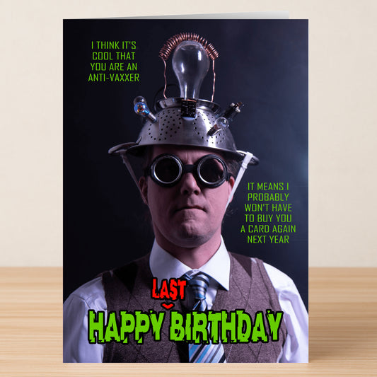 A man in a suit, goggles, and a wired colander hat stands before the Twisted Gifts Anti-vaxxer Funny Birthday Card, known for its sarcastic humor.
