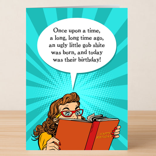 The Gobshite Funny Birthday Card by Twisted Gifts features a cartoon woman in red glasses, holding a "Happy Birthday" book with witty humor: “Once upon a time, an ugly little gob shite was born, and today was their birthday!”.