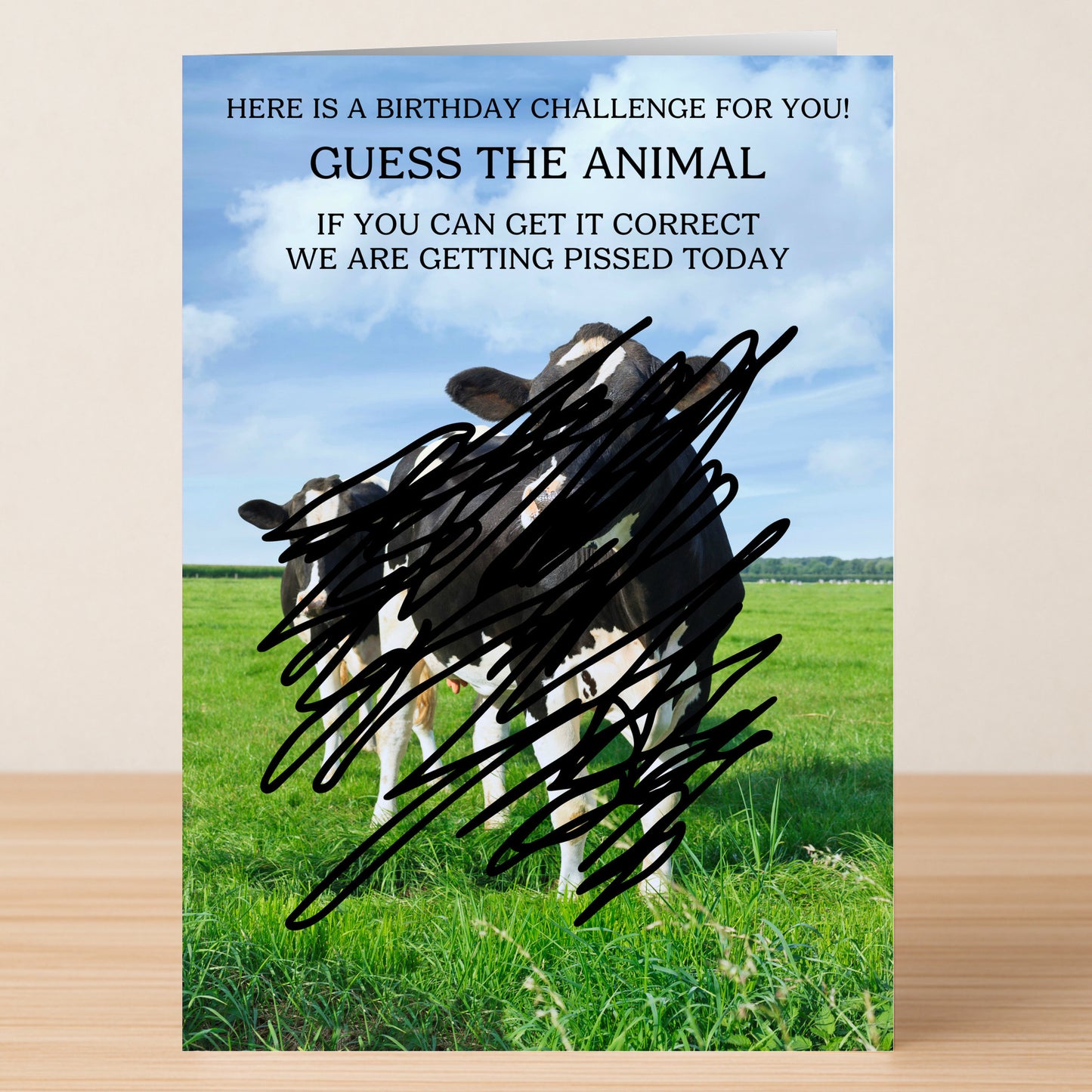 The Guess The Animal Funny Birthday Card by Twisted Gifts features cows in a field, partly hidden by black scribbles, and invites you to guess the animal for a witty and humorous birthday greeting.
