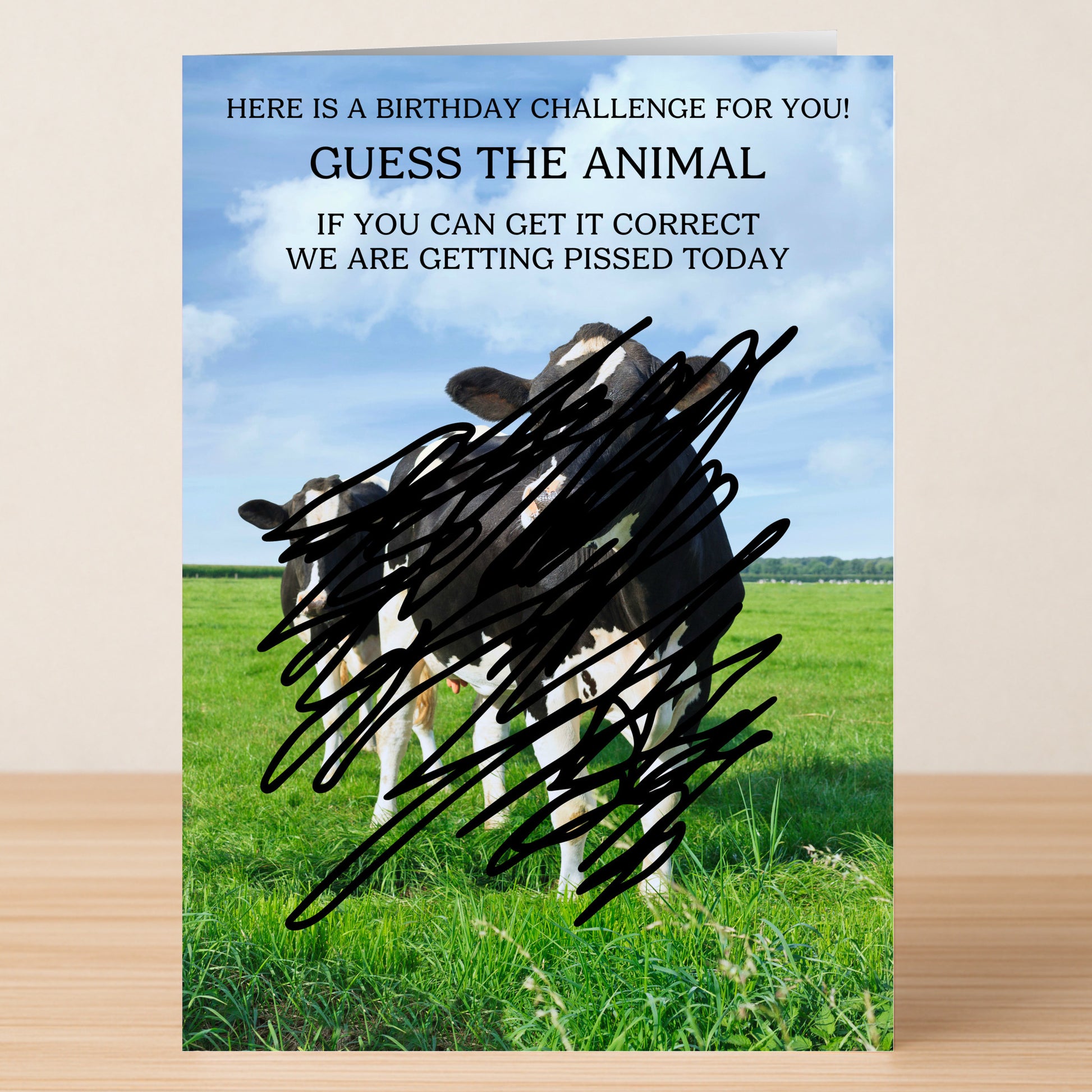 The Guess The Animal Funny Birthday Card by Twisted Gifts features cows in a field, partly hidden by black scribbles, and invites you to guess the animal for a witty and humorous birthday greeting.
