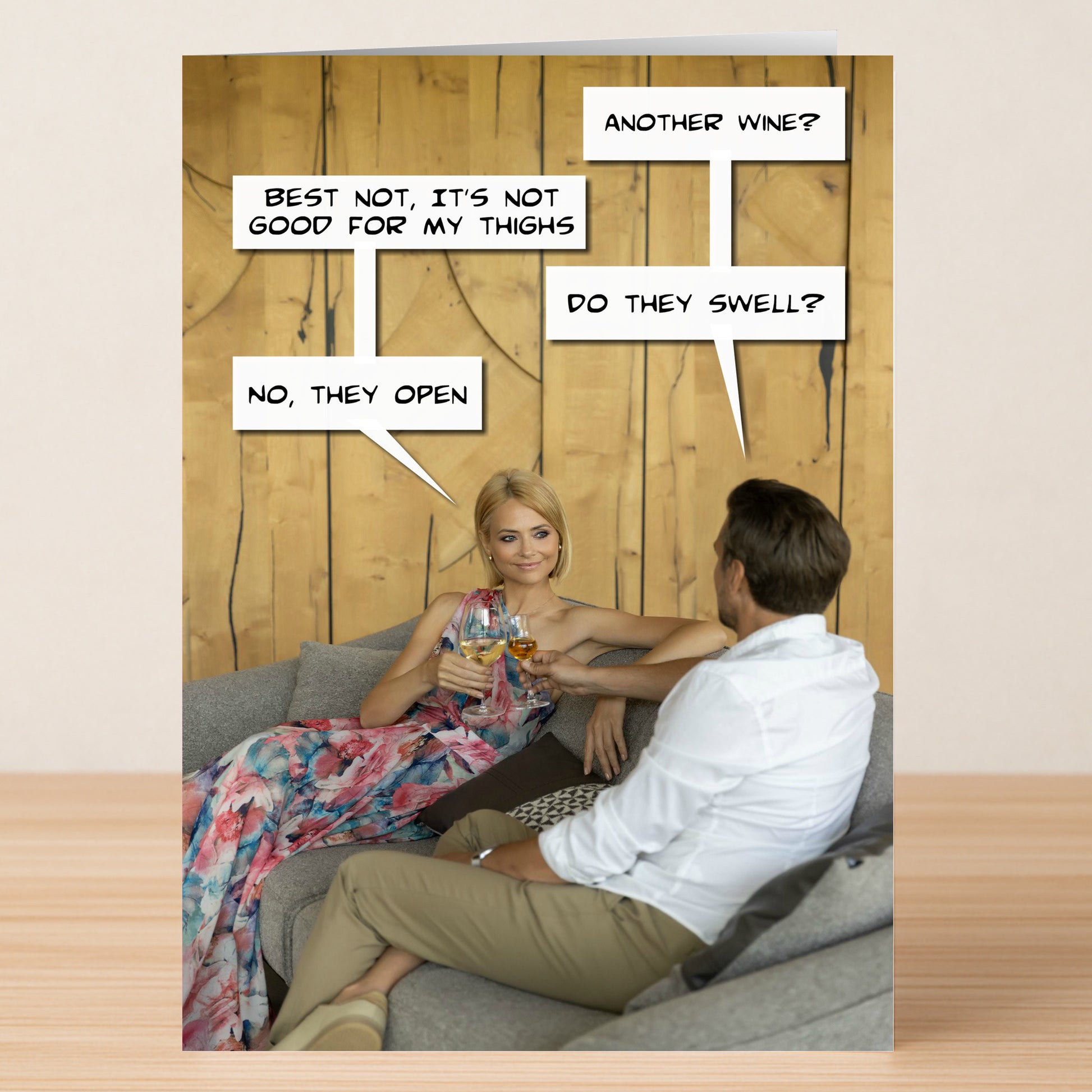 A woman in a floral dress and a man in a white shirt sit on a couch, clinking wine glasses with funny speech bubbles about wine and thighs—Twisted Gifts’ Thighs Funny Birthday Card is perfect for anyone with a quirky sense of humor.