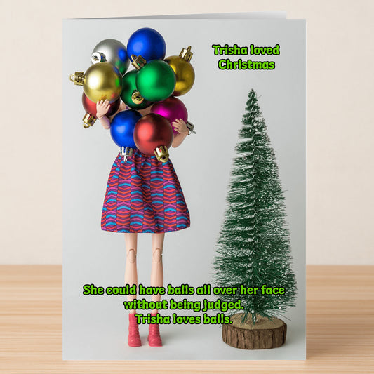 The Loves Balls Rude Christmas Card by Twisted Gifts shows a doll with her face covered by colorful Christmas ornaments beside a small artificial tree. This cheeky card is perfect for spreading laughs during the holiday season.