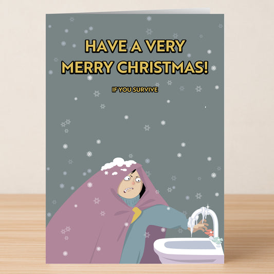 The Survive Funny Christmas Card by Twisted Gifts shows a cartoon in a coat running cold water over their hands with snow falling, plus the text: "Have a very merry Christmas! If you survive." Perfect for anyone who loves hilarious holiday cards.