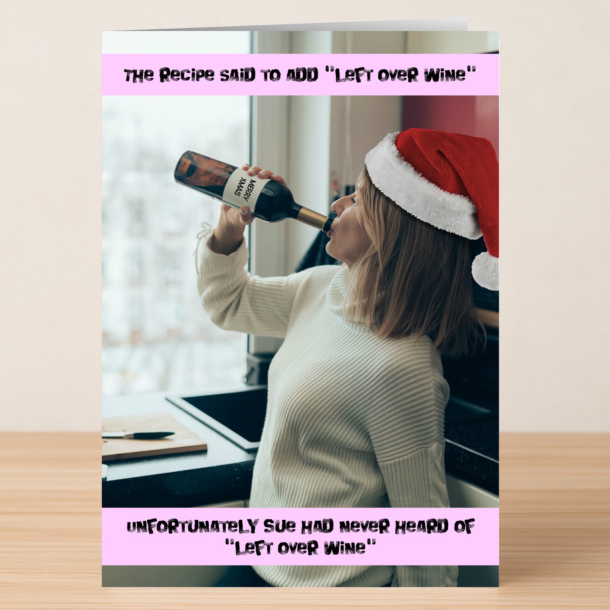 A woman in a Santa hat drinks wine in her kitchen, joking about never having leftover wine for recipes. The "Left Over Wine Funny Christmas Card" by Twisted Gifts is the perfect humorous card for the holidays.