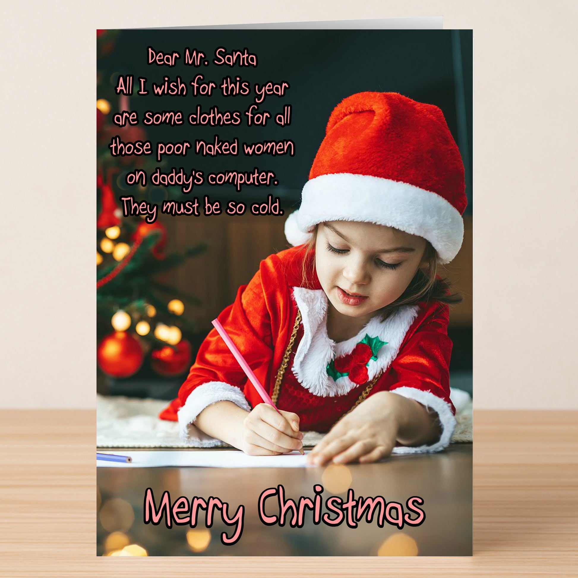A young girl in a Santa outfit writes at a table by the tree on this "Daddy's Computer Funny Christmas Card" from Twisted Gifts—a hilarious pick for tech-savvy dads who need clothes for their computer images.
