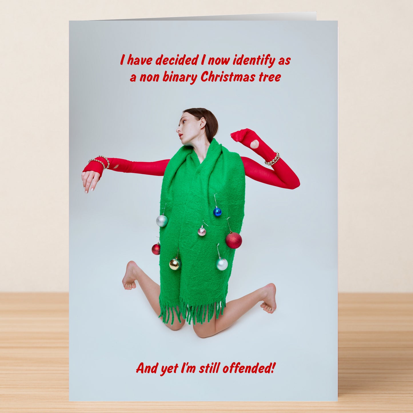 Person poses with a green scarf and red sleeves, featured as a non-binary Christmas tree—offended for the holidays. Twisted Gifts' Non Binary Christmas Card is perfect for an inclusive or funny holiday greeting!.