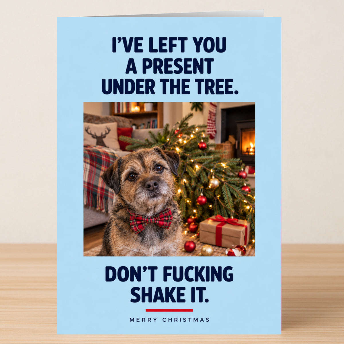 Under The Tree - Funny Christmas Card featuring a dog in a bow tie sitting by a tree with a gift and the text, “I’VE LEFT YOU A PRESENT UNDER THE TREE. DON’T FUCKING SHAKE IT. MERRY CHRISTMAS.”