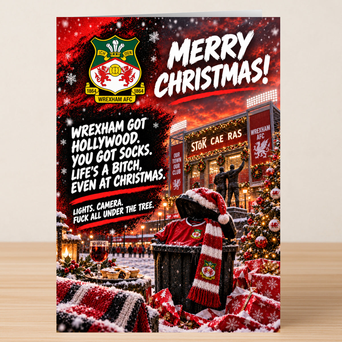 Wrexham AFC – Funny Christmas Card featuring the team logo, a stadium at sunset, festive decorations, and the text: “Merry Christmas! Wrexham got Hollywood. You got socks. Life’s a bitch.”