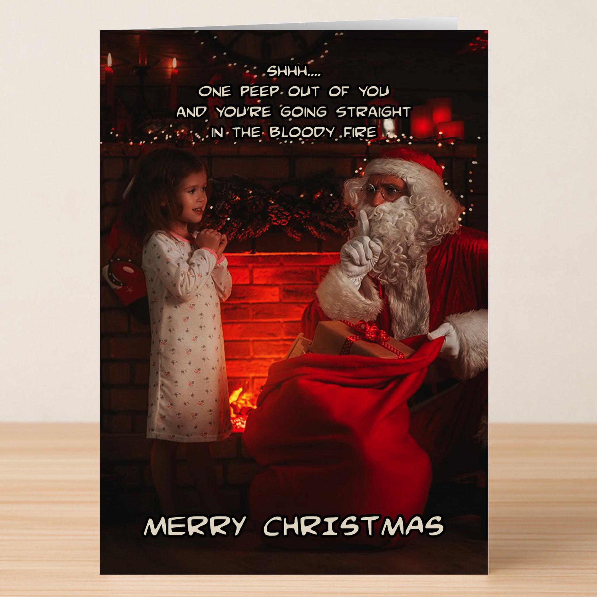 A young girl stands with Santa near a fireplace on the Twisted Gifts "Bloody Fire Funny Christmas Card," where Santa hushes her as a darkly funny message and "Merry Christmas" add twisted holiday cheer.
