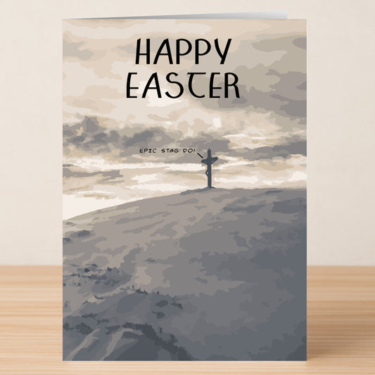 The Epic Funny Easter Card by Twisted Gifts sits on a wooden surface, featuring a cross silhouette on a hill under cloudy skies with "HAPPY EASTER" at the top—perfect for celebrating Easter.