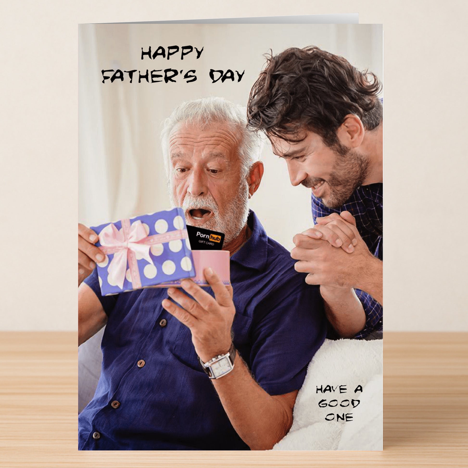 An older man looks surprised while opening a Twisted Gifts 'Gift Card Funny Father's Day Card' with a younger man smiling beside him. The card reads "Happy Father's Day" and "Have a good one," adding humor to the moment.
