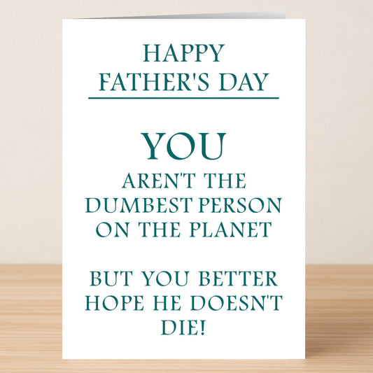The Dumb Insulting Father's Day Card by Twisted Gifts sits on a wooden surface, featuring the playful message: "Happy Father's Day. You aren't the dumbest person on the planet, but you better hope he doesn't die!.