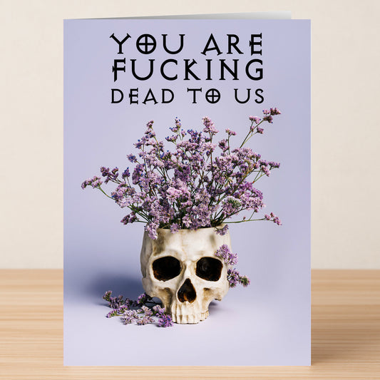 The Dead To Us Funny Farewell Card by Twisted Gifts features a skull with purple flowers and the bold phrase "YOU ARE FUCKING DEAD TO US"—a perfect humorous goodbye card for fans of dark humor.