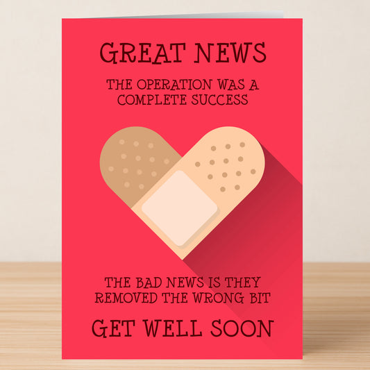 The Wrong Bit Funny Get Well Soon Card by Twisted Gifts sits on a wooden surface, showing a heart made of bandages and the message: “Great news: The operation was a success. Bad news—they removed the wrong bit. Speedy Recovery—get well soon!”.