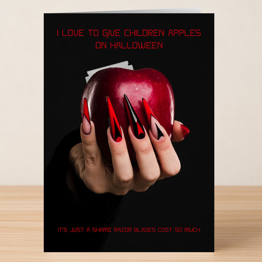 The Apples Funny Halloween Card by Twisted Gifts features a hand with long red and black nails holding an apple with razor blades—a humorous Halloween card poking fun at the classic "razor blade in apples" joke.