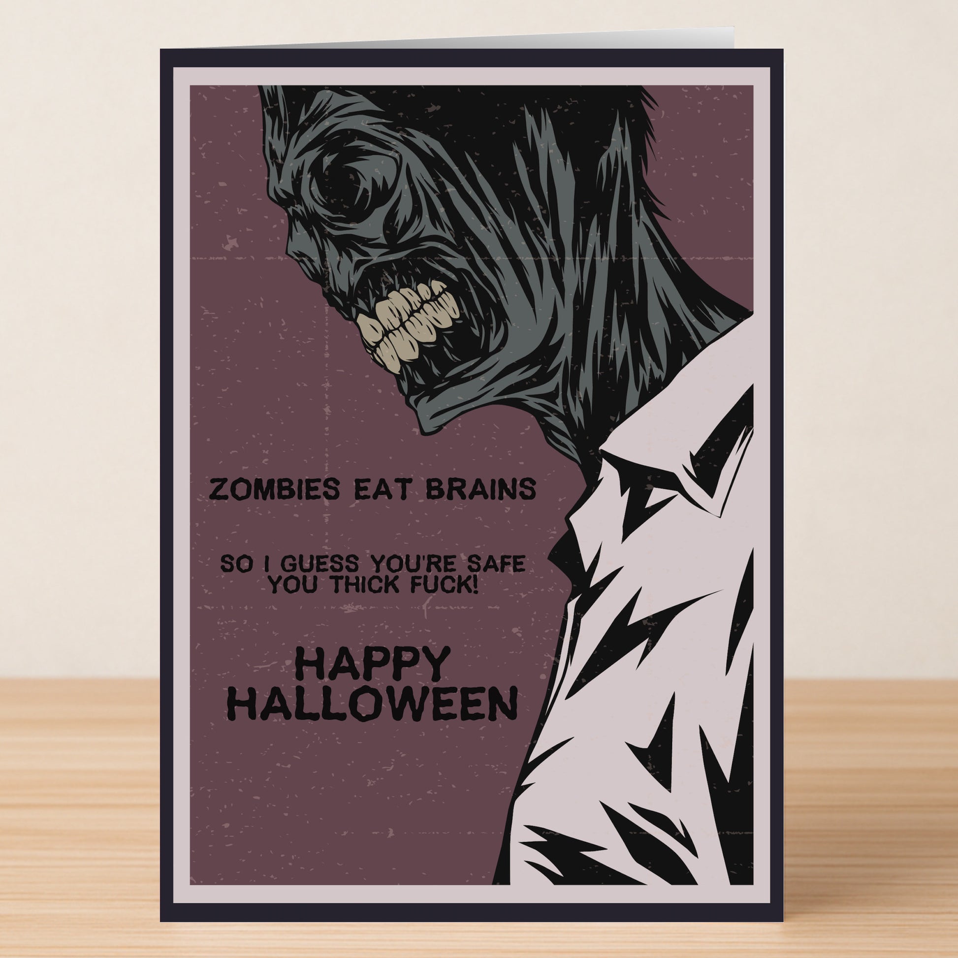 The Eat Brains Insulting Halloween Card from Twisted Gifts features a zombie and the phrase "Zombies eat brains so I guess you’re safe. Happy Halloween." Ideal for spooky celebrations, it comes displayed on a wooden surface.