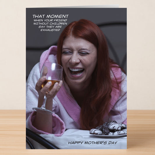 A woman in a bathrobe laughs with a wine glass, featuring the text: "That moment when your friend without children says they're exhausted." Send this Twisted Gifts That Moment Funny Mother's Day Card to share some humor!.