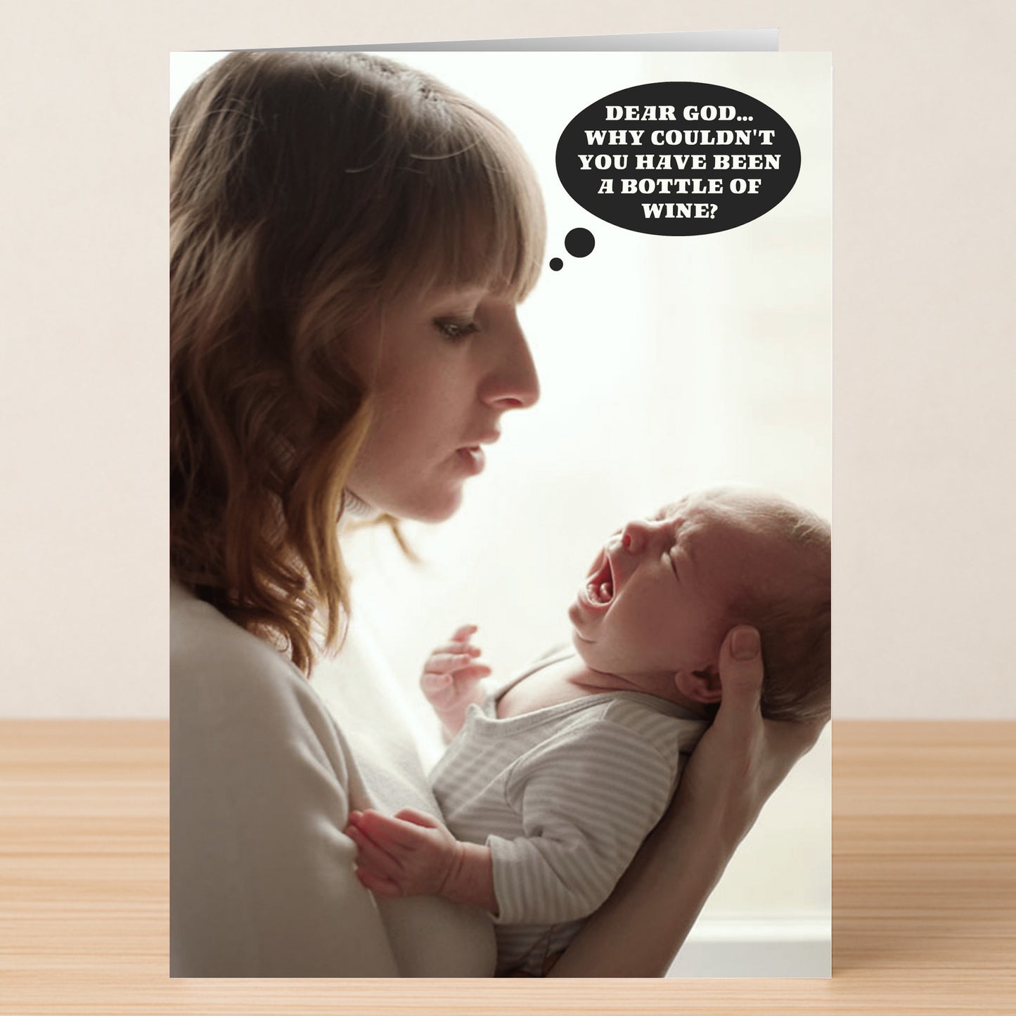A woman holds a crying baby, gazing at it as a thought bubble says, "Dear God... Why couldn't you have been a bottle of wine?"—the Dear God Funny Mother's Day Card by Twisted Gifts is the perfect quirky and humorous greeting card.
