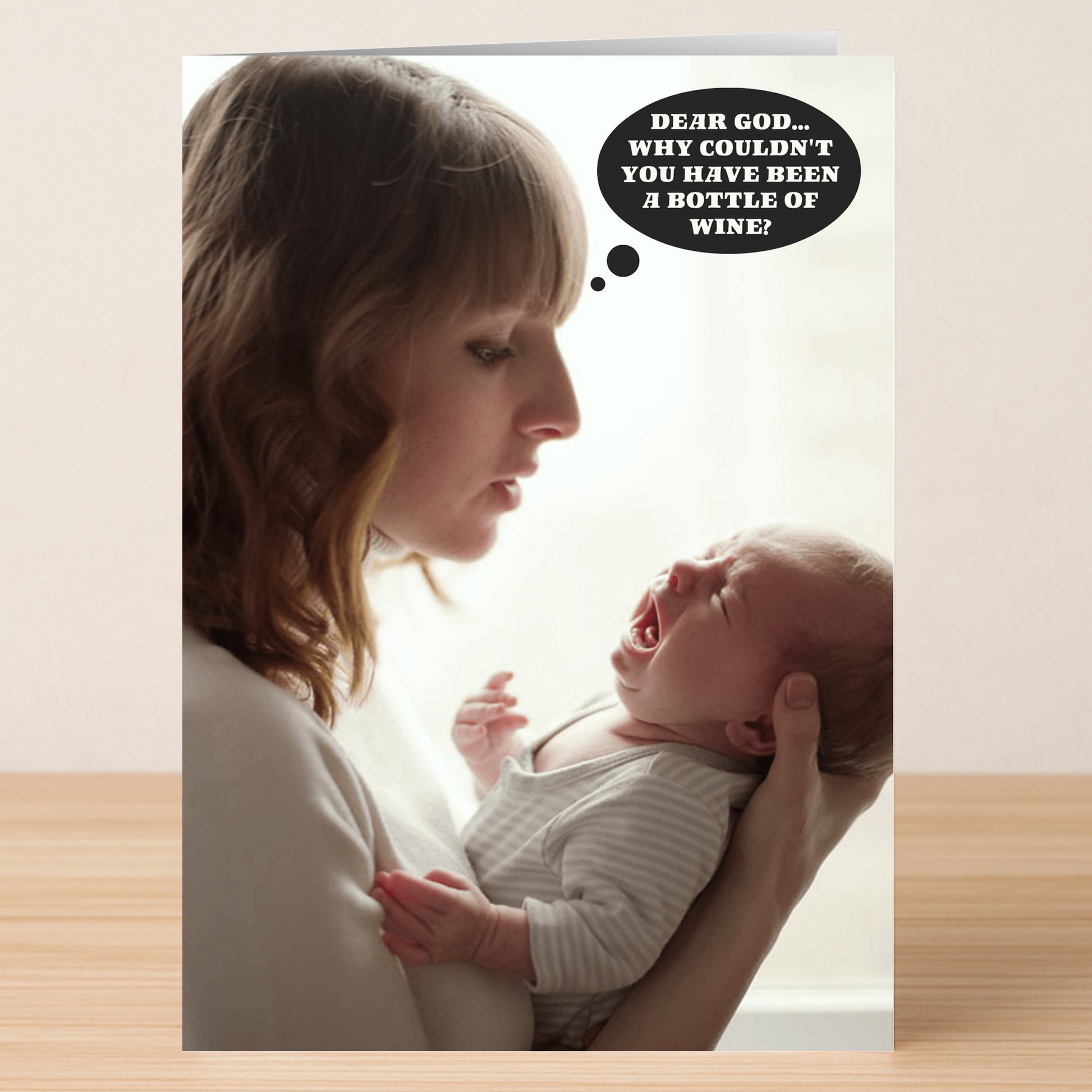 A woman holds a crying baby, gazing at it as a thought bubble says, "Dear God... Why couldn't you have been a bottle of wine?"—the Dear God Funny Mother's Day Card by Twisted Gifts is the perfect quirky and humorous greeting card.