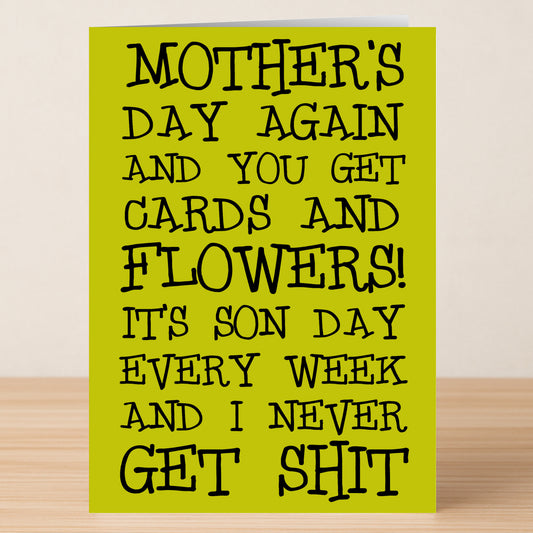 The Twisted Gifts Son Day Funny Mother's Day Card rests on a wooden surface, featuring the message: "MOTHER'S DAY AGAIN AND YOU GET CARDS AND FLOWERS! IT'S SON DAY EVERY WEEK AND I NEVER GET SHIT." A perfect humorous card for mom.