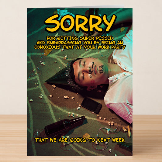 A man in a party hat lies on the floor with doodles on his face, beer bottles, popcorn, and a phone nearby. The Twisted Gifts Obnoxious Rude Sorry Card delivers a hilarious apology for being obnoxiously rude at the work party!.