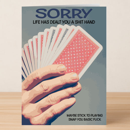 A hand holds the Shit Hand Insulting Sorry Card from Twisted Gifts—a bold card reading, "SORRY LIFE HAS DEALT YOU A SHIT HAND. MAYBE STICK TO PLAYING SNAP YOU BASIC FUCK," perfect for anyone with sharp humor and sass.