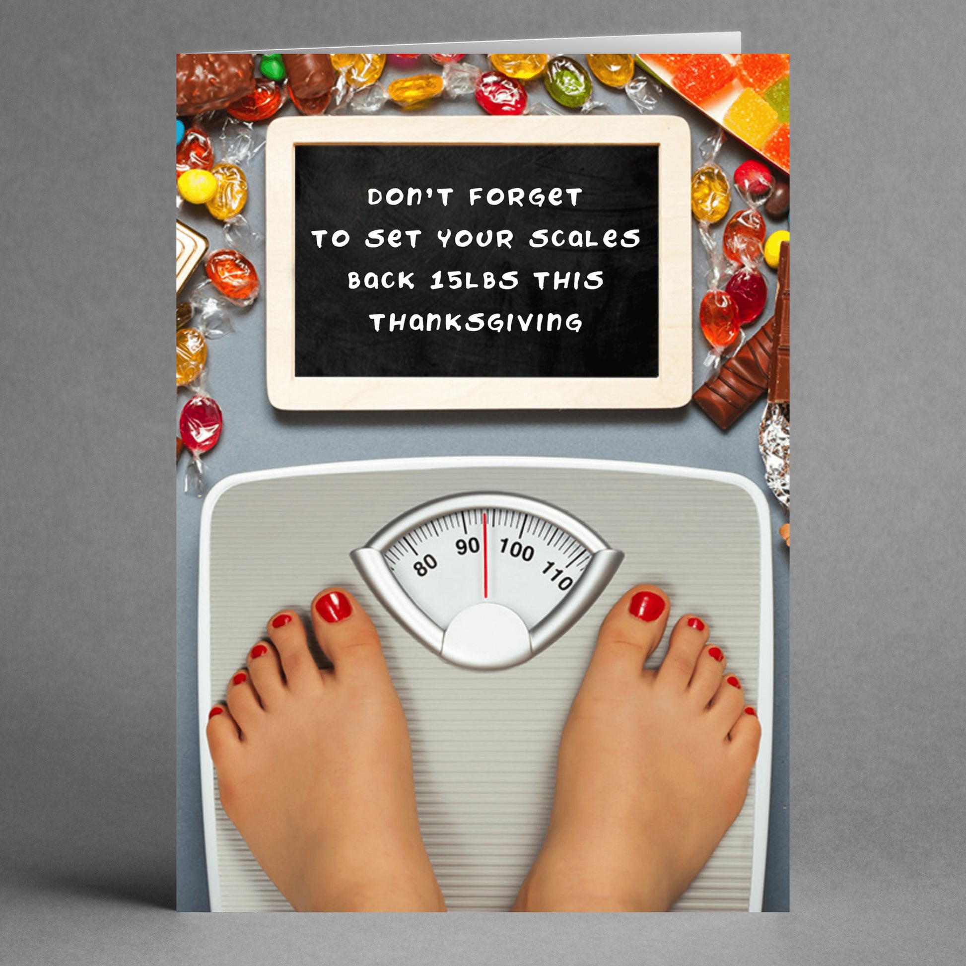 The *Set Your Scales Insulting Thanksgiving Card* by Twisted Gifts features a humorous design perfect for the holiday season. It shows a scale with bare feet and a sarcastic sign surrounded by candy that reads, "Don't forget to set your scales back 15 lbs this Thanksgiving." Ideal for those who enjoy a touch of humor during the festivities.