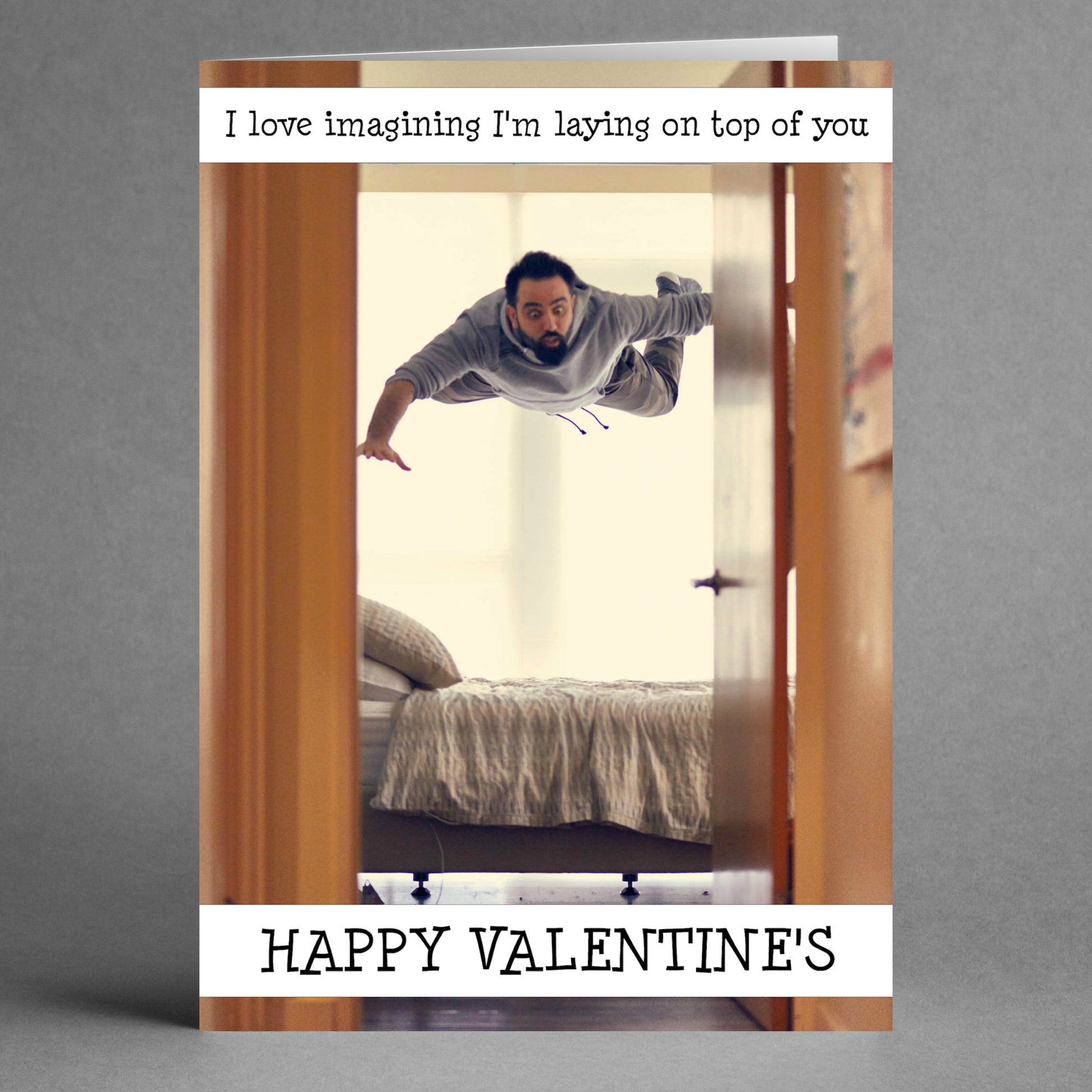 A man is horizontally suspended in mid-air, appearing to fly towards a bed in a room. The playful message says, "I love imagining I'm laying on top of you." The On Top Rude Valentine's Card by Twisted Gifts perfectly captures the spirit of the romantic holiday.