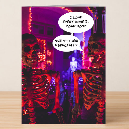 Two skeletons with speech bubbles—one says, "I love every bone in your body," the other replies, "One of them especially." Fun purple and orange lights. Twisted Gifts' Bones Funny Valentine's Card is perfect for a quirky Valentine!.