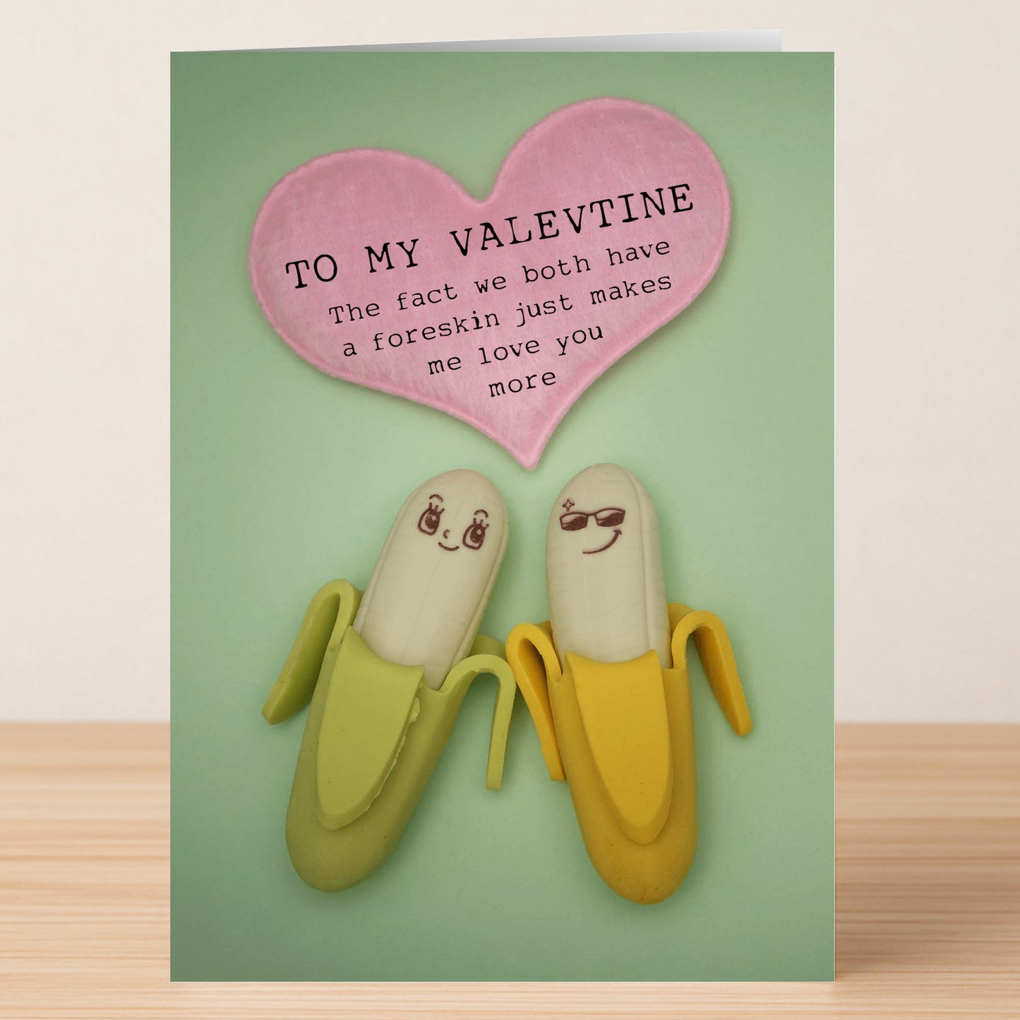 Two bananas with cute faces sit under a pink heart reading, "TO MY VALENTINE: The fact we both have a foreskin just makes me love you more." A cheeky twist from Twisted Gifts' Both Of Us Insulting Valentine's Card.