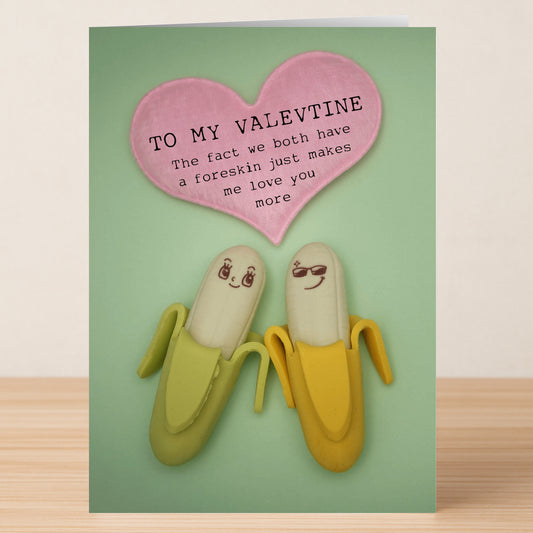Two bananas with cute faces sit under a pink heart reading, "TO MY VALENTINE: The fact we both have a foreskin just makes me love you more." A cheeky twist from Twisted Gifts' Both Of Us Insulting Valentine's Card.