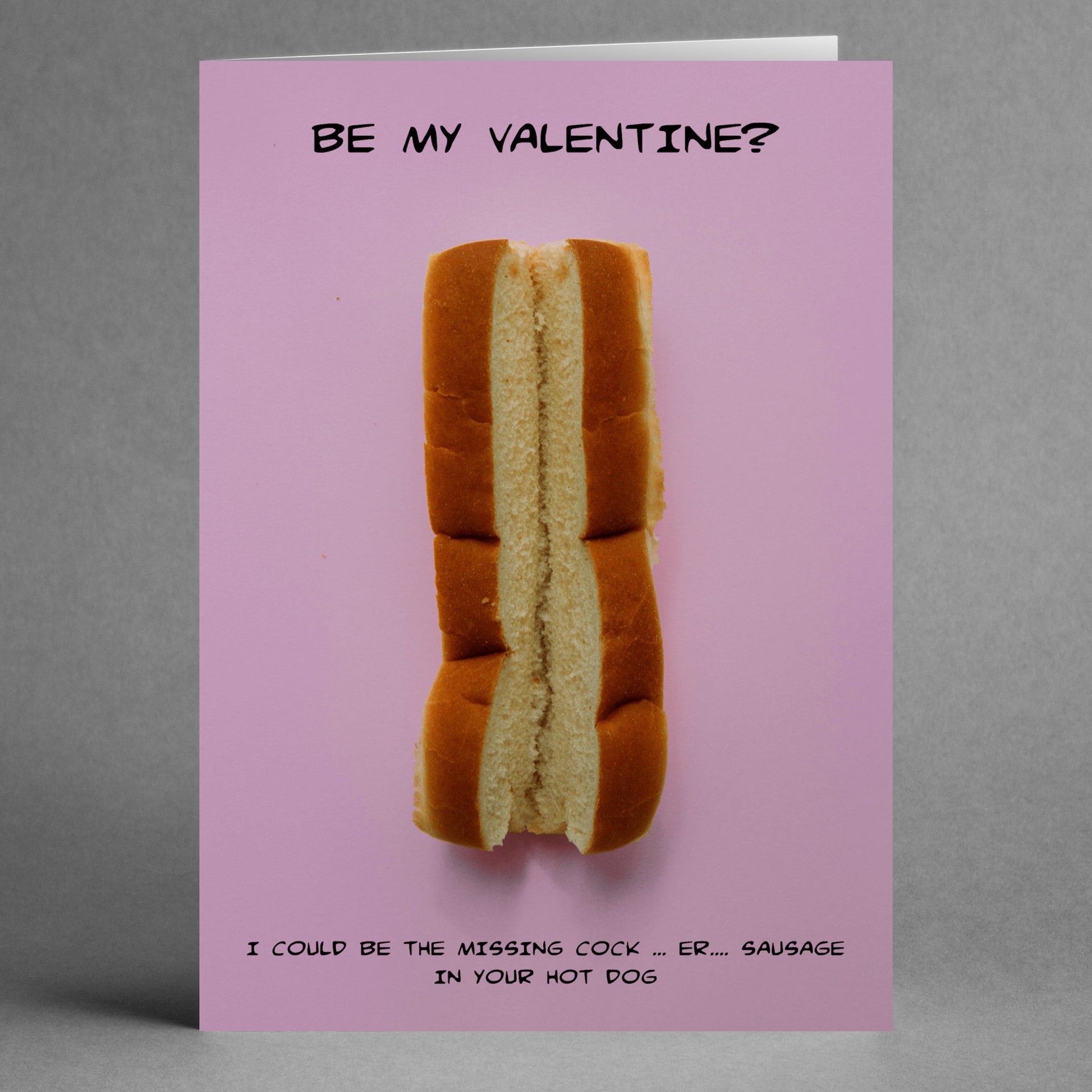 The Hot Dog Funny Valentine's Card by Twisted Gifts features a unique design with a hot dog bun on a pink background, along with the witty text: "BE MY VALENTINE? I COULD BE THE MISSING COCK... ER... SAUSAGE IN YOUR HOT DOG." This card is ideal for those who enjoy clever humor.