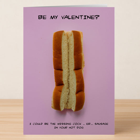 The Hot Dog Funny Valentine's Card by Twisted Gifts features a hot dog bun on pink with playful text: "Be my Valentine?" above and "I could be the missing cock...er...sausage in your hot dog." Ideal for fans of witty humor.