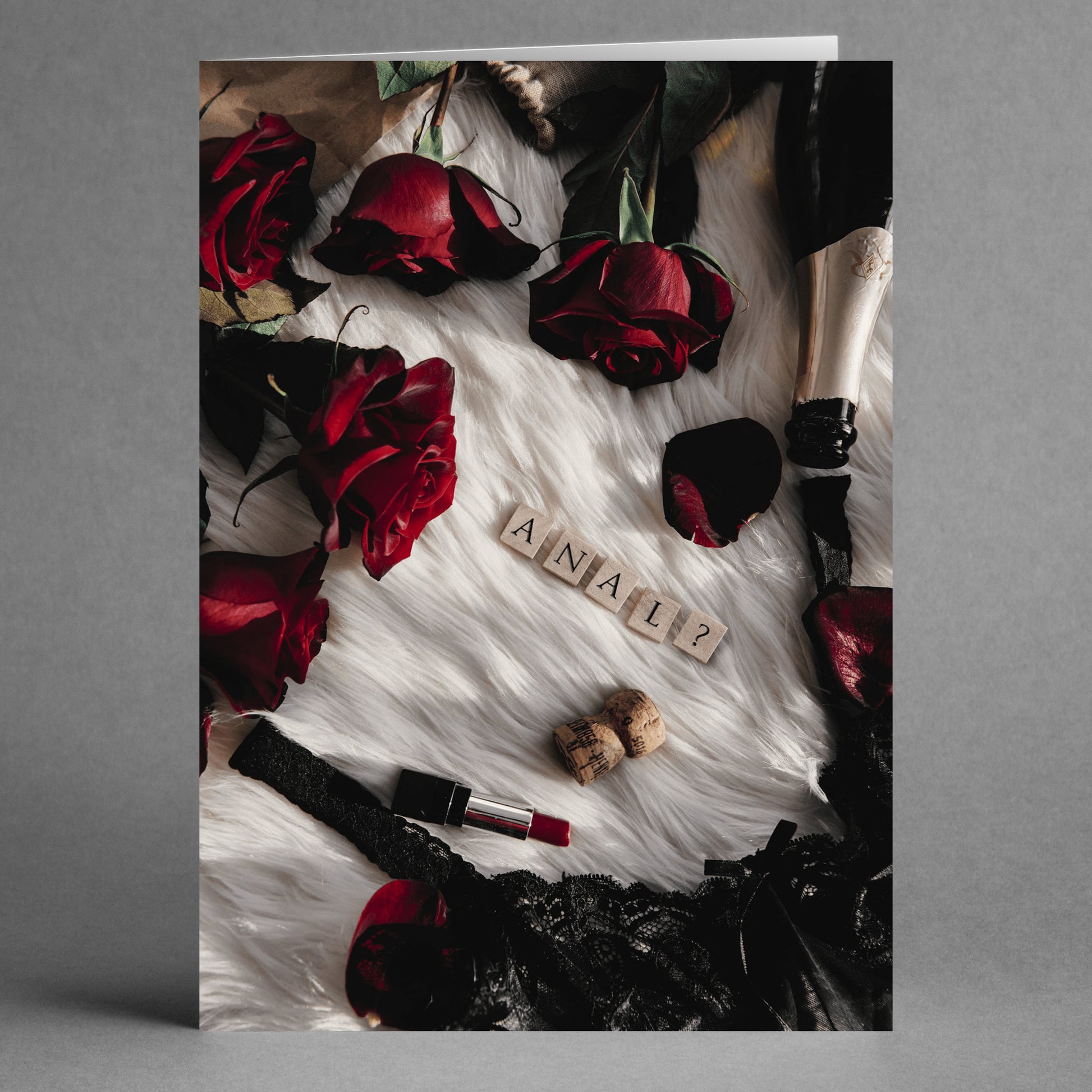 Create a playful Valentine's setup with Twisted Gifts' Champagne and Roses Rude Valentine's Card. Featuring dark roses, a champagne bottle, lipstick, lace, and letter tiles on white fur that unexpectedly spell "ANAL?", this card balances elegance with humor for an unforgettable evening.