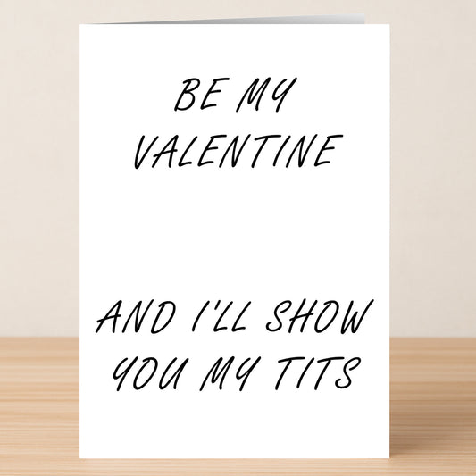 The Tits Rude Valentine's Card by Twisted Gifts is a white card with black handwritten text: "BE MY VALENTINE AND I'LL SHOW YOU MY TITS," shown upright on a wooden surface.
