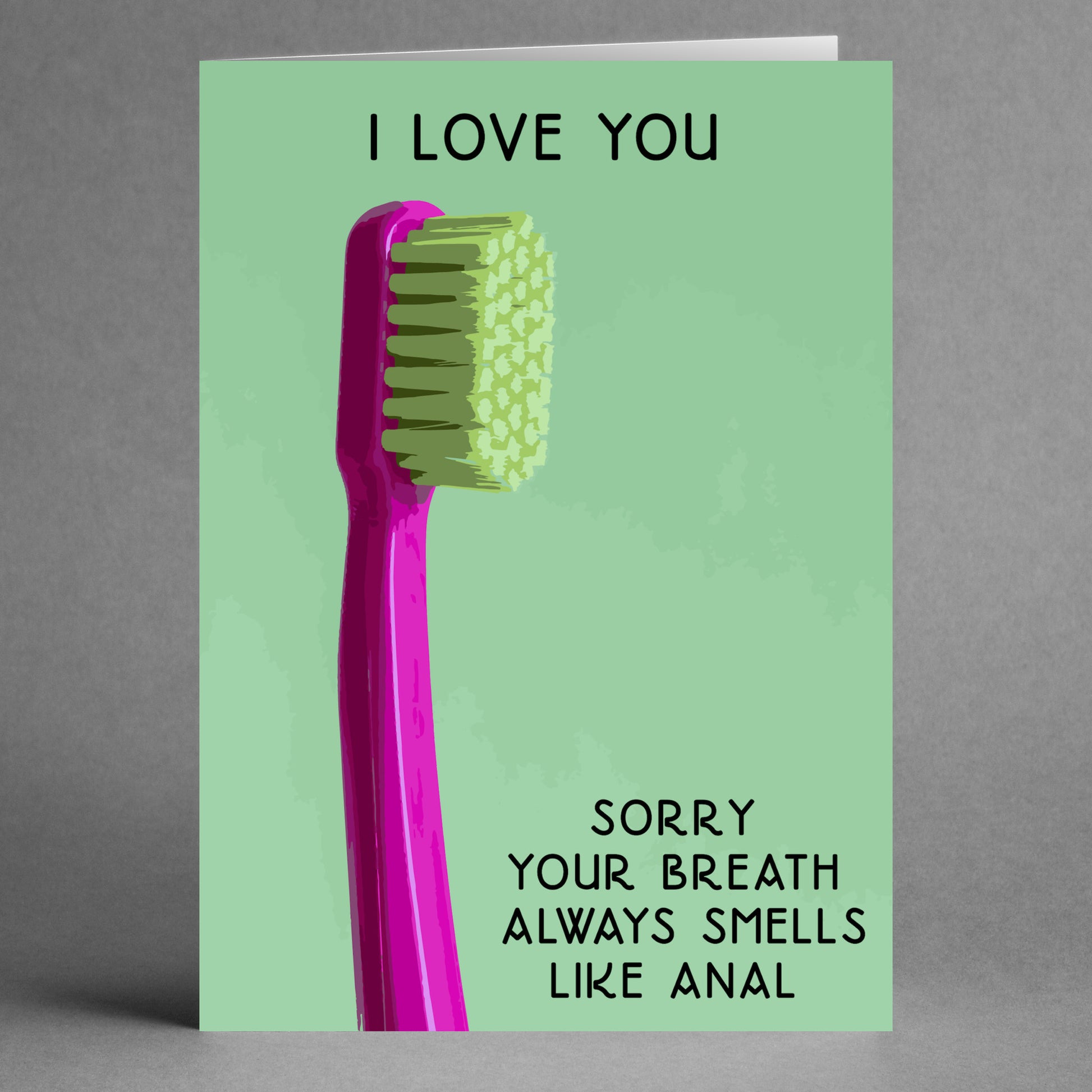 The Breath Twisted Valentine's Card by Twisted Gifts showcases a pink toothbrush against a green background, with the message: "I love you. Sorry your breath always smells like anal." It's ideal for those who enjoy subversive humor and want to send a cheeky message with a twist.