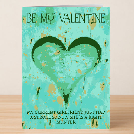The Munter Insulting Valentine's Card by Twisted Gifts features a green heart on blue and the cheeky message: "BE MY VALENTINE. MY CURRENT GIRLFRIEND JUST HAD A STROKE SO NOW SHE IS A RIGHT MUNTER." Ideal for a laugh!.
